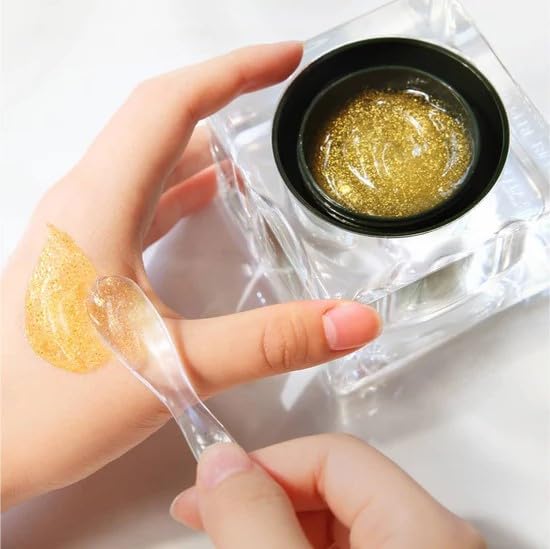 Gold gel being applied with a spoon onto a hand, with a container of gold gel in the background.