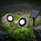 Two stone-like solar lights on grass with a third one showing the solar panel.
