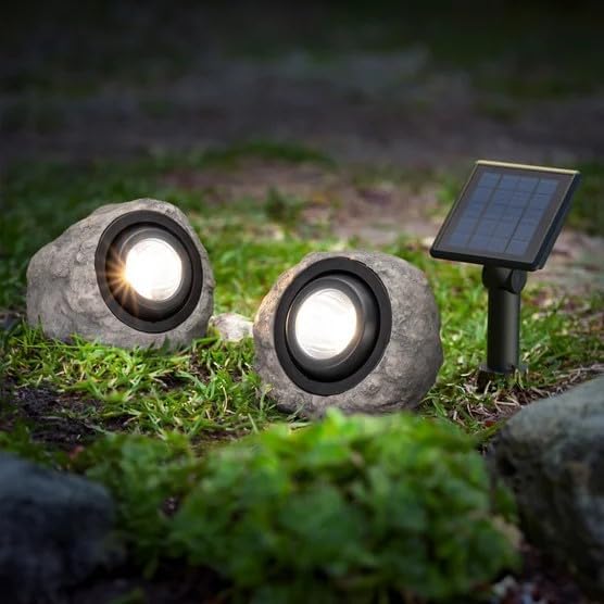 Two stone-like solar lights on grass with a third one showing the solar panel.