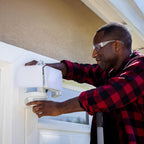 Person installing a security camera on a house exterior