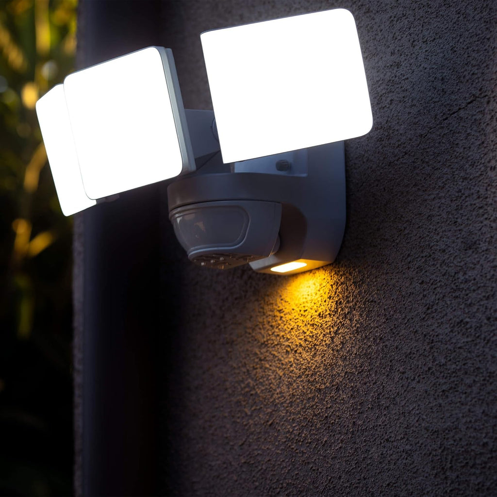 Outdoor security light fixture on a wall with two bright white lights and one yellow light.