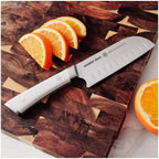 Knife with white handle on a wooden cutting board next to sliced oranges