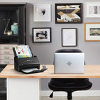 Epson scanner on a desk with a laptop, surrounded by framed pictures on the wall.