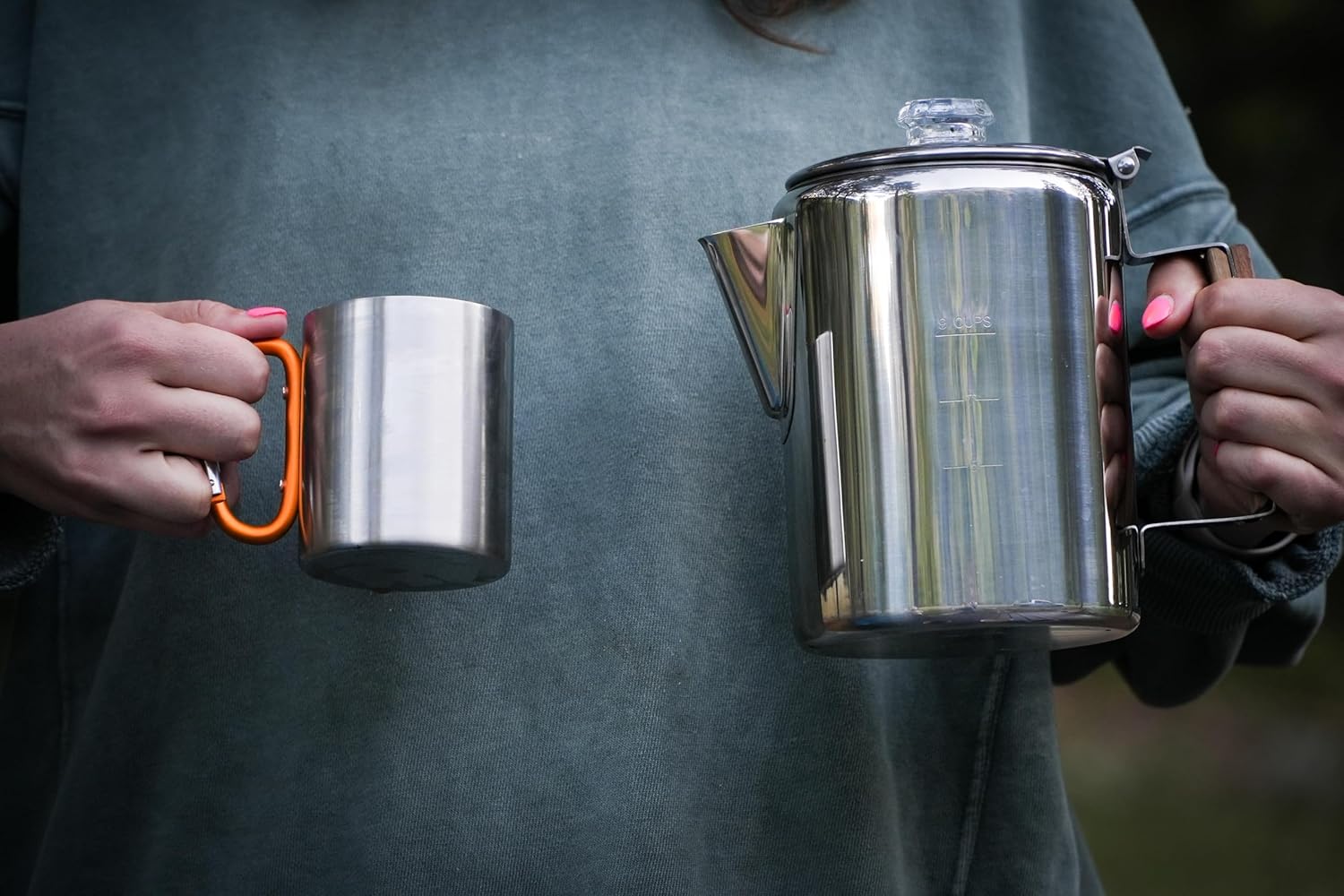 Person holding a metal mug and a metal kettle with a blurred background