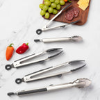 Set of kitchen tongs on a marble surface with vegetables and a cutting board in the background.